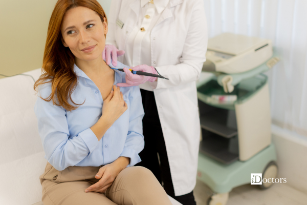 Donna che ha una mano sulla spalla per tenere la camicia con dietro una dottoressa che ha in mano uno strumento.