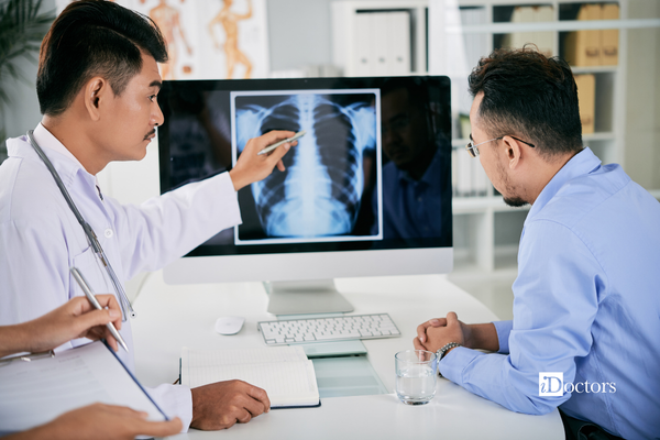 Medico che mostra una rx del torace a un paziente seduti davanti al computer.