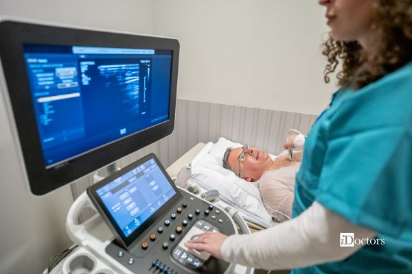 Paziente sottoposto a ecocardiogramma durante una visita cardiologica, con sonda sul torace e immagini del cuore sul monitor.