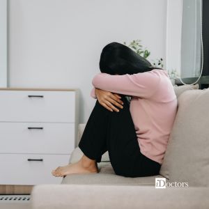 Persona seduta sul divano con le ginocchia al petto e il volto nascosto in atteggiamento di ansia.