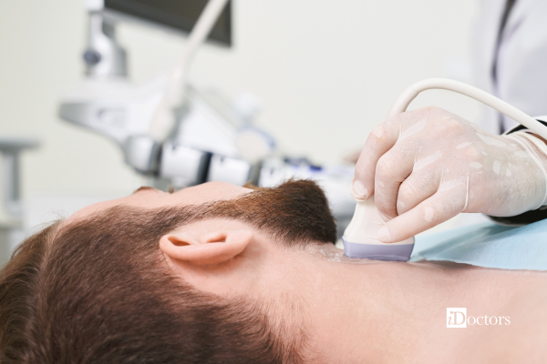 Medico che tiene in mano una sonda poggiata sul collo parzialmente ricoperto di gel di un paziente