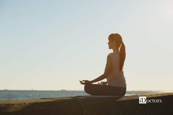 Donna seduta in meditazione davanti al mare durante una pratica di mindfulness.