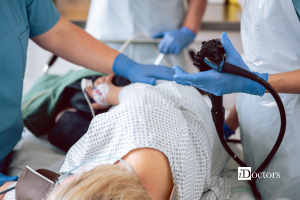Paziente sdraiato su un lettino con intorno dei medici che hanno in mano un colonscopio.
