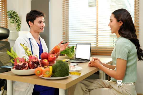Medico con davanti la paziente, tra di loro un tavolo con sopra un pc, della frutta e della verdura.