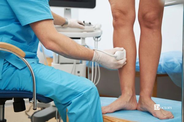 Medico esegue un’ecografia della gamba durante una visita flebologica, con il paziente in piedi.