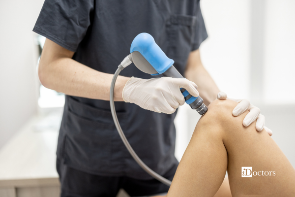 Professionista che esegue una seduta di onde d'urto sul ginocchio di una paziente.